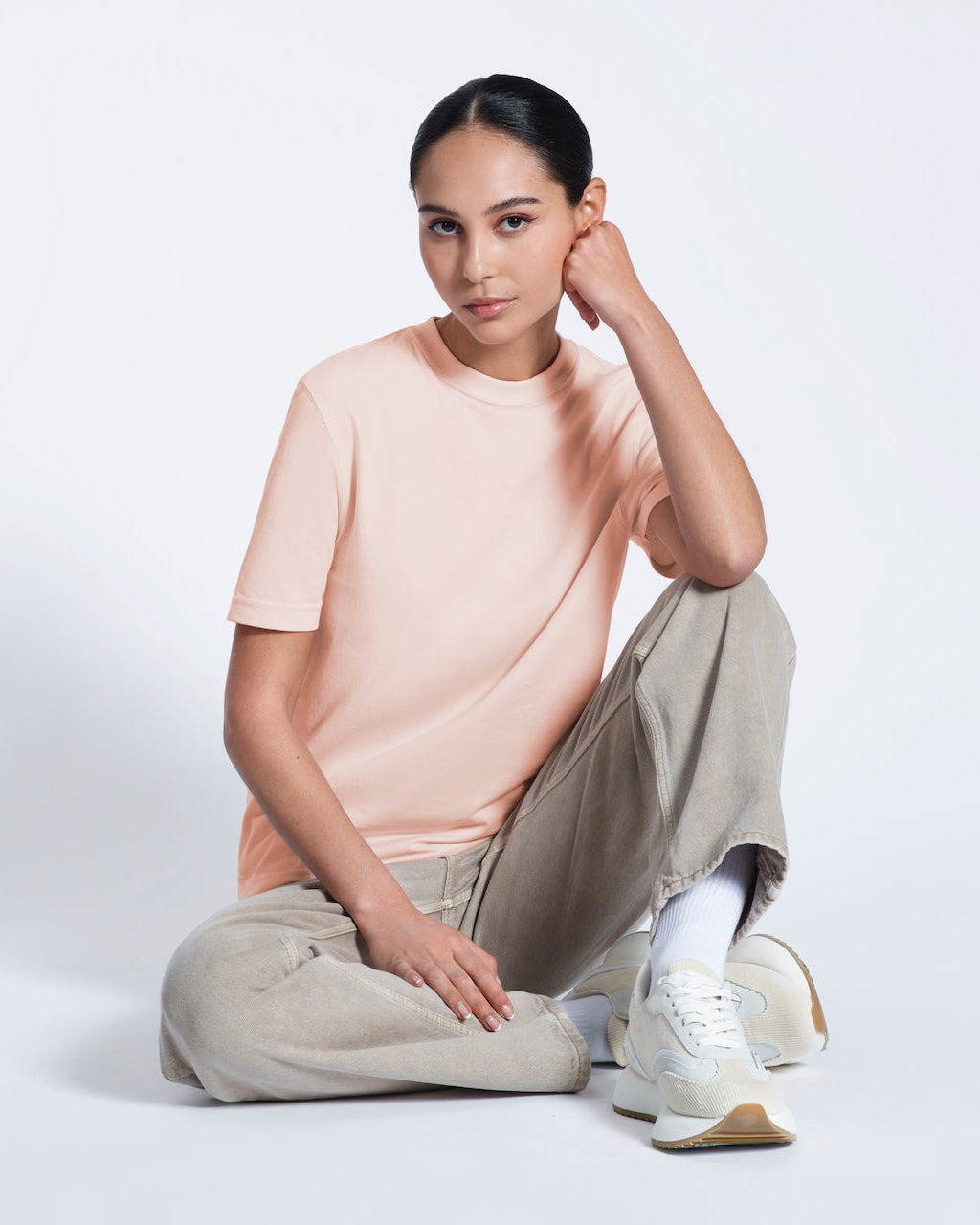A woman sitting on the floor looking into the camera, modelling a plain pink short sleeve organic cotton t shirt.