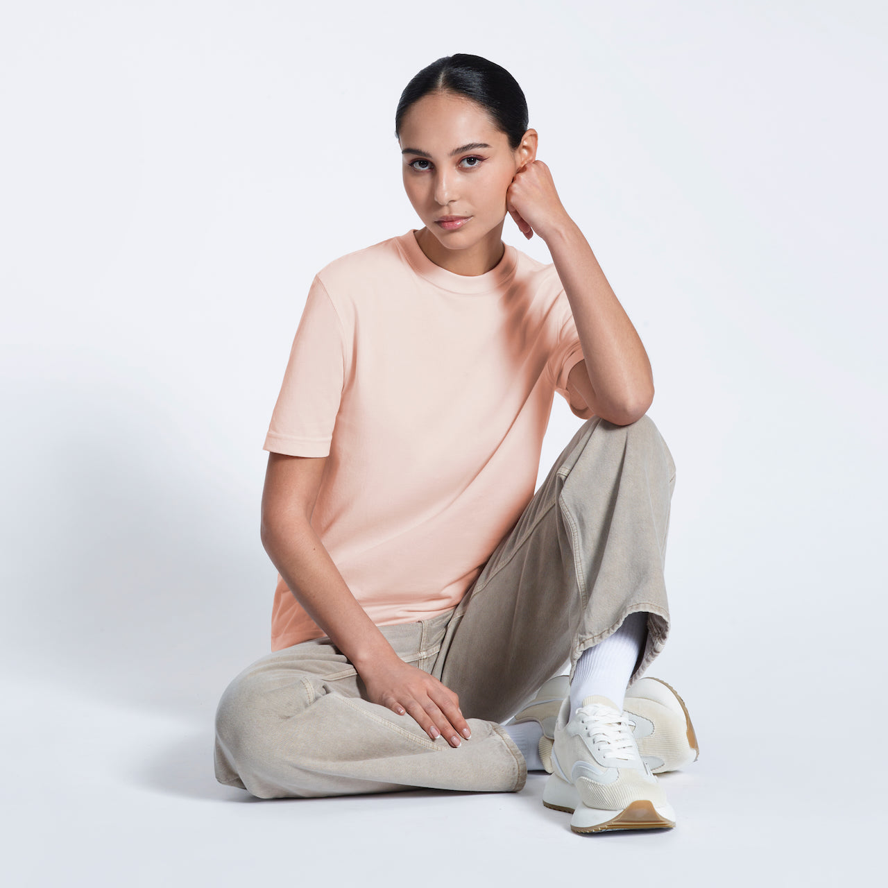 A woman sitting on the floor looking into the camera, modelling a plain pink short sleeve organic cotton t shirt.