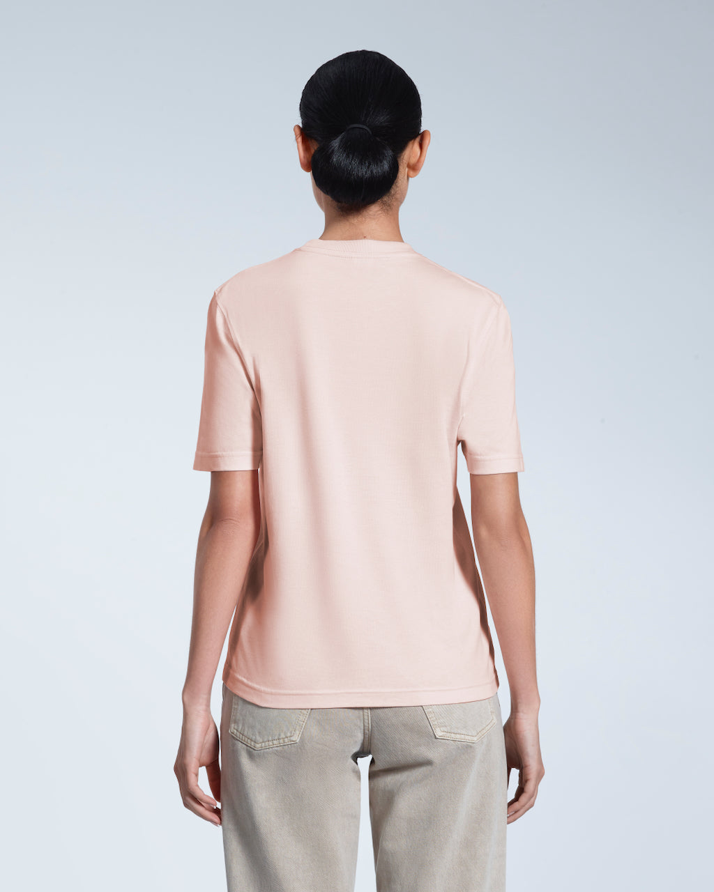 A woman with her back to the camera, modelling a plain pink short sleeve organic cotton t shirt.
