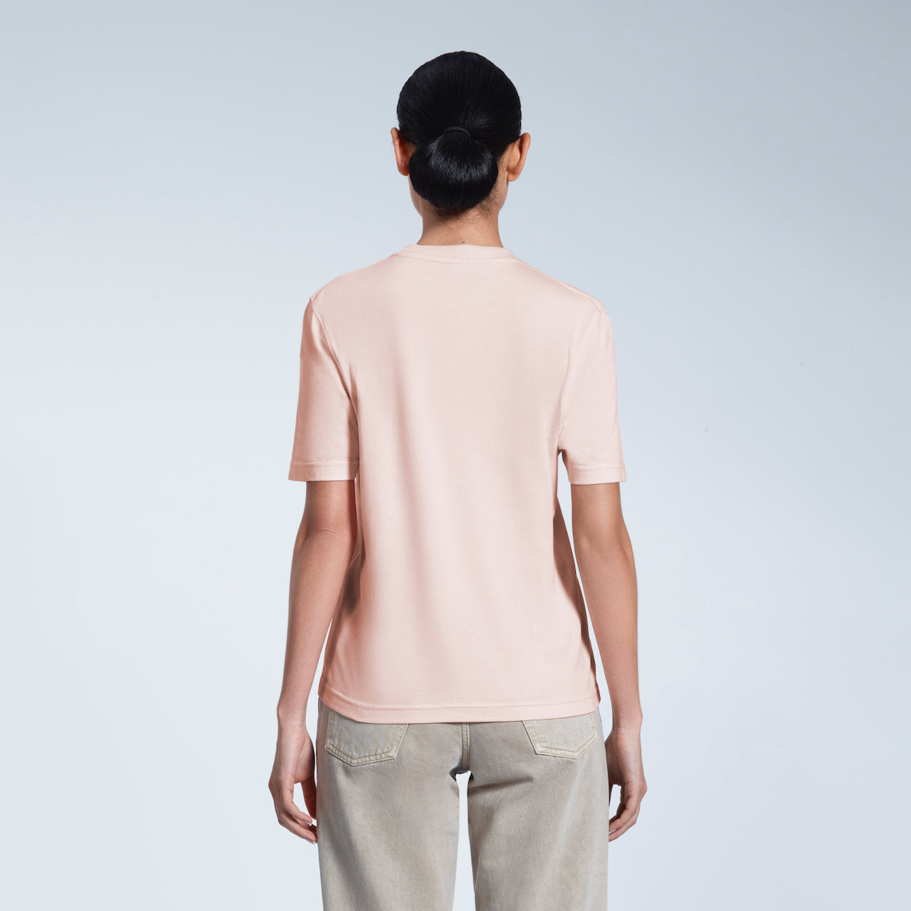 A woman with her back to the camera, modelling a plain pink short sleeve organic cotton t shirt.