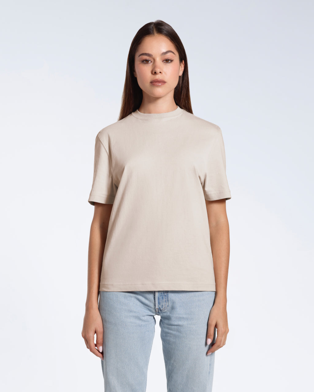 A woman facing front on looking at the camera, modelling a stone coloured short sleeve organic cotton t shirt.