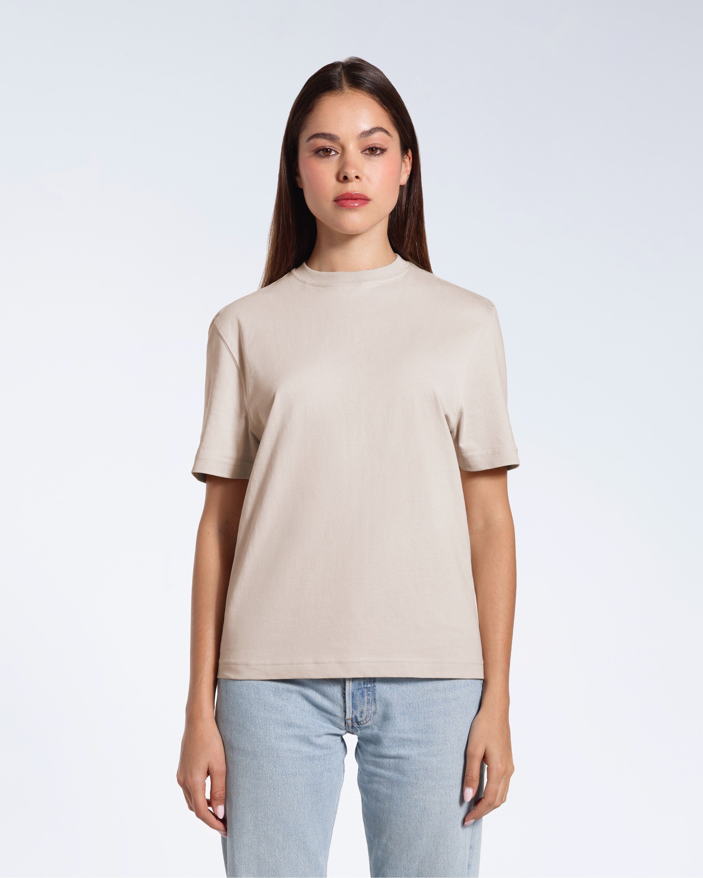 A woman facing front on looking at the camera, modelling a stone coloured short sleeve organic cotton t shirt.