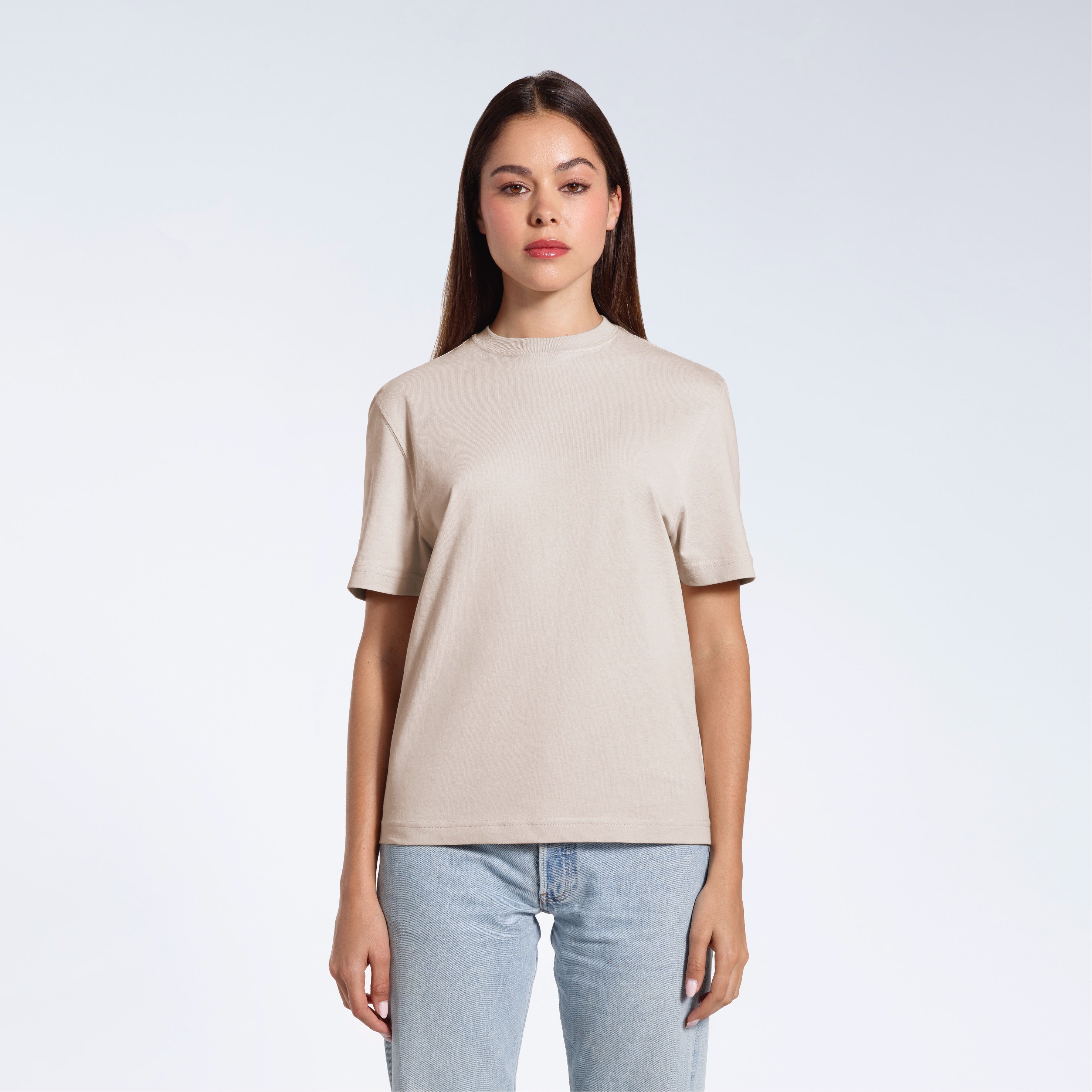 A woman facing front on looking at the camera, modelling a stone coloured short sleeve organic cotton t shirt.