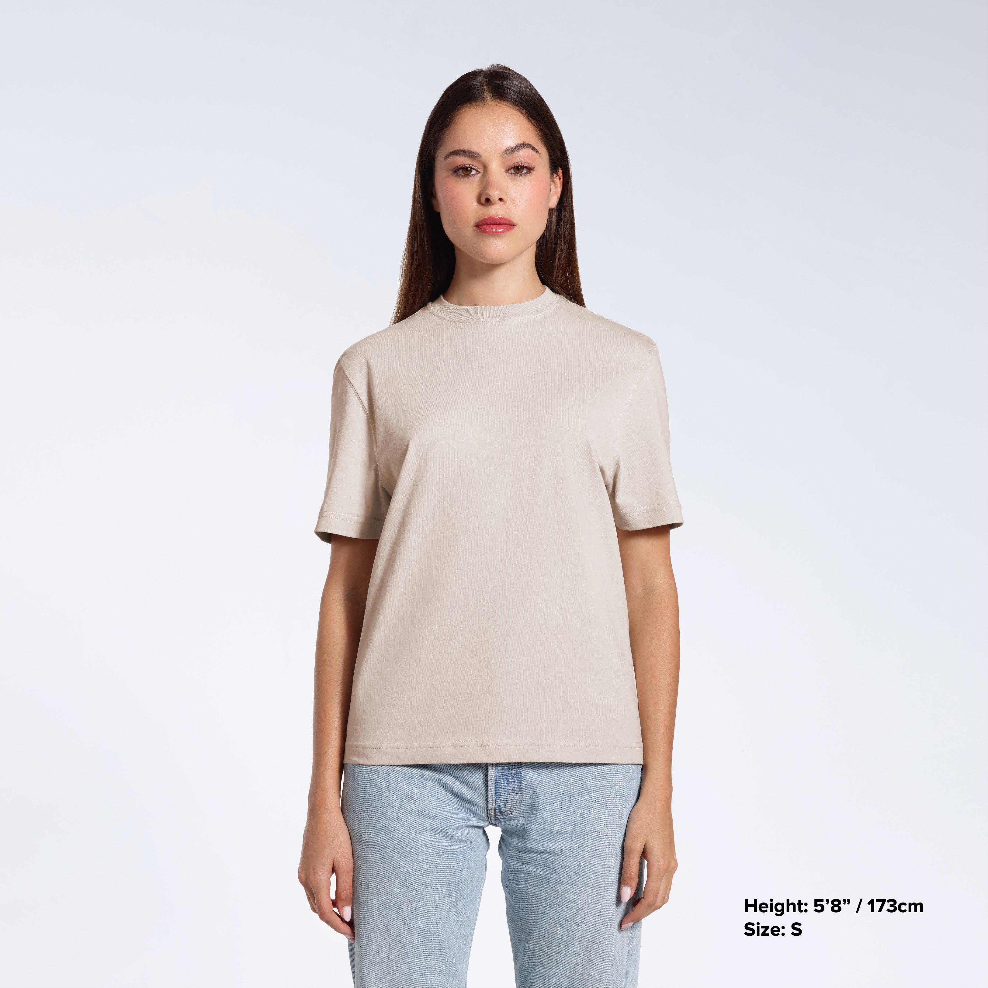 A woman facing front on looking at the camera, modelling a stone coloured short sleeve organic cotton t shirt.