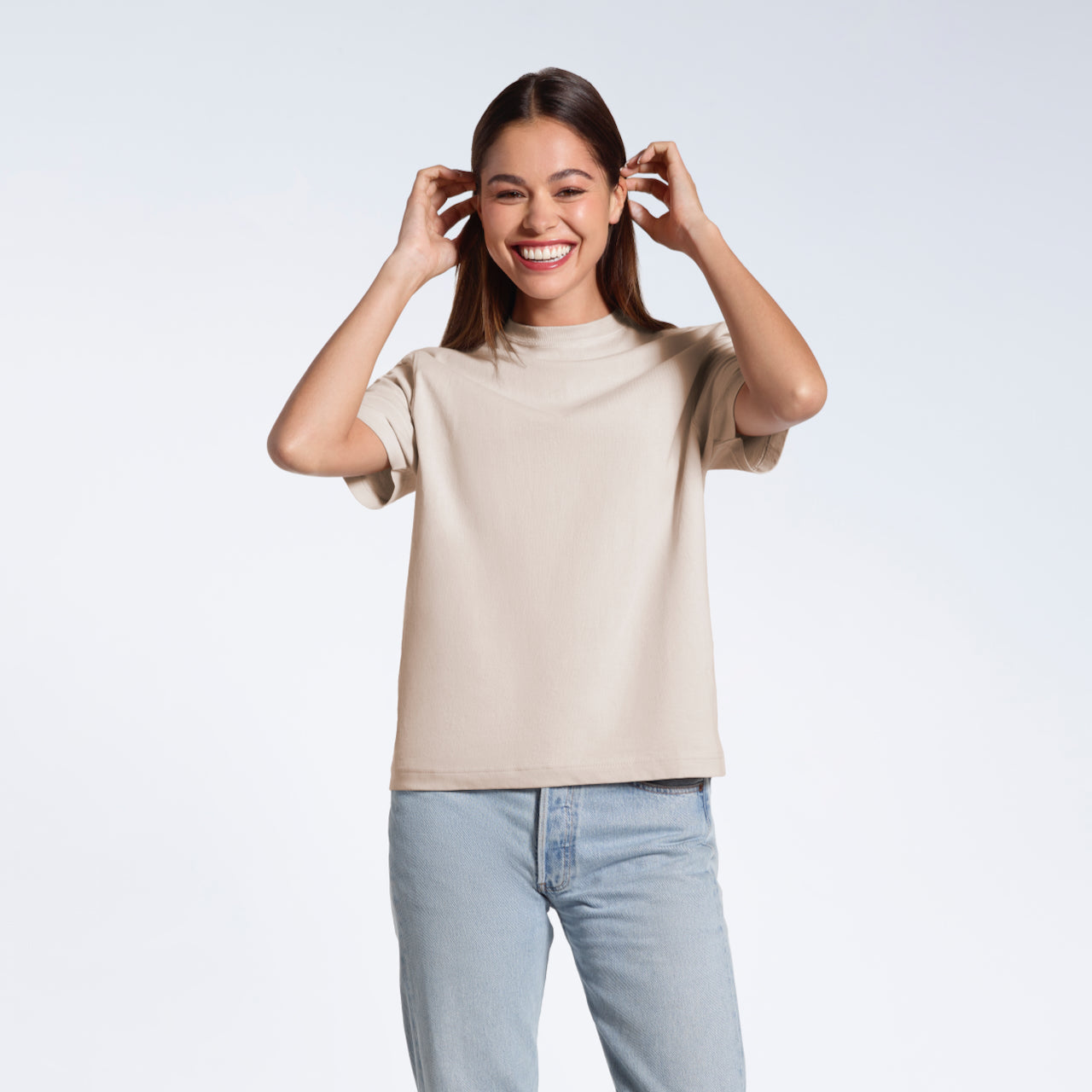 A woman smiling tucking her hair behind her ears, modelling a plain pink short sleeve organic cotton t shirt.
