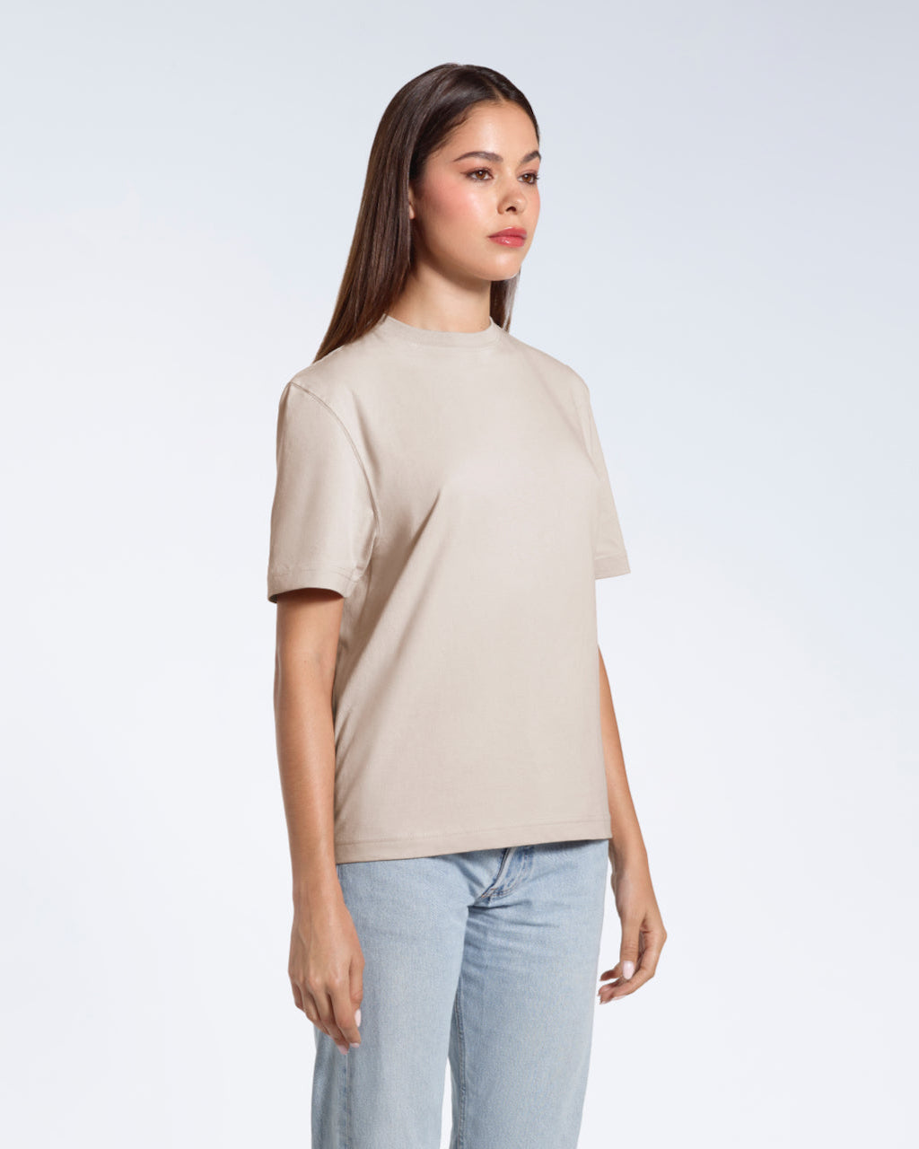 A woman standing at an angle with her arms by her sides, modelling a plain stone coloured short sleeve organic cotton t shirt.