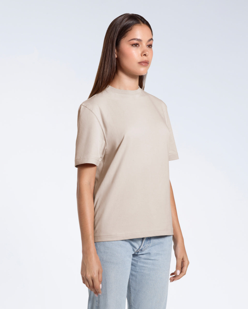 A woman standing at an angle with her arms by her sides, modelling a plain stone coloured short sleeve organic cotton t shirt.