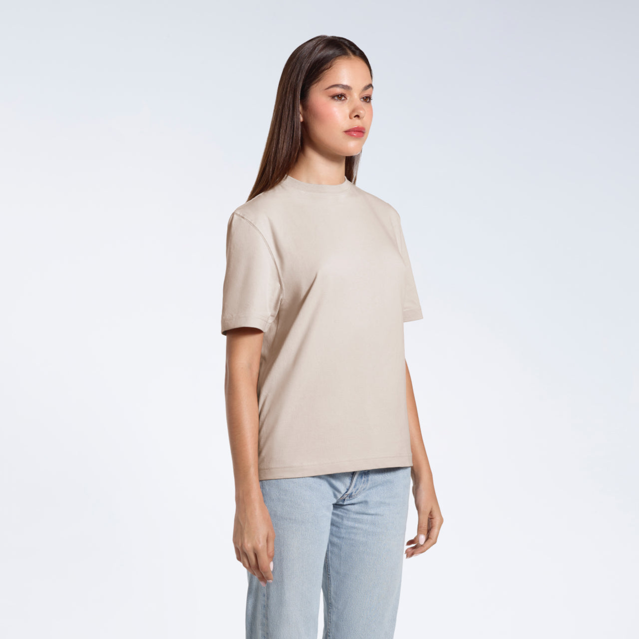 A woman standing at an angle with her arms by her sides, modelling a plain stone coloured short sleeve organic cotton t shirt.
