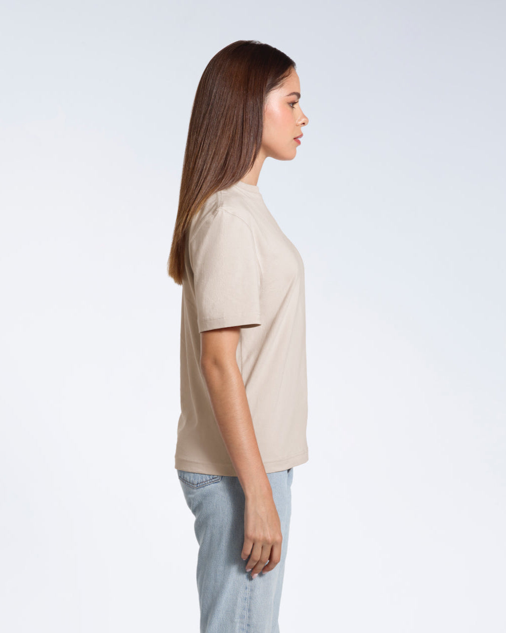 A woman facing side on, modelling a plain stone coloured short sleeve organic cotton t shirt.