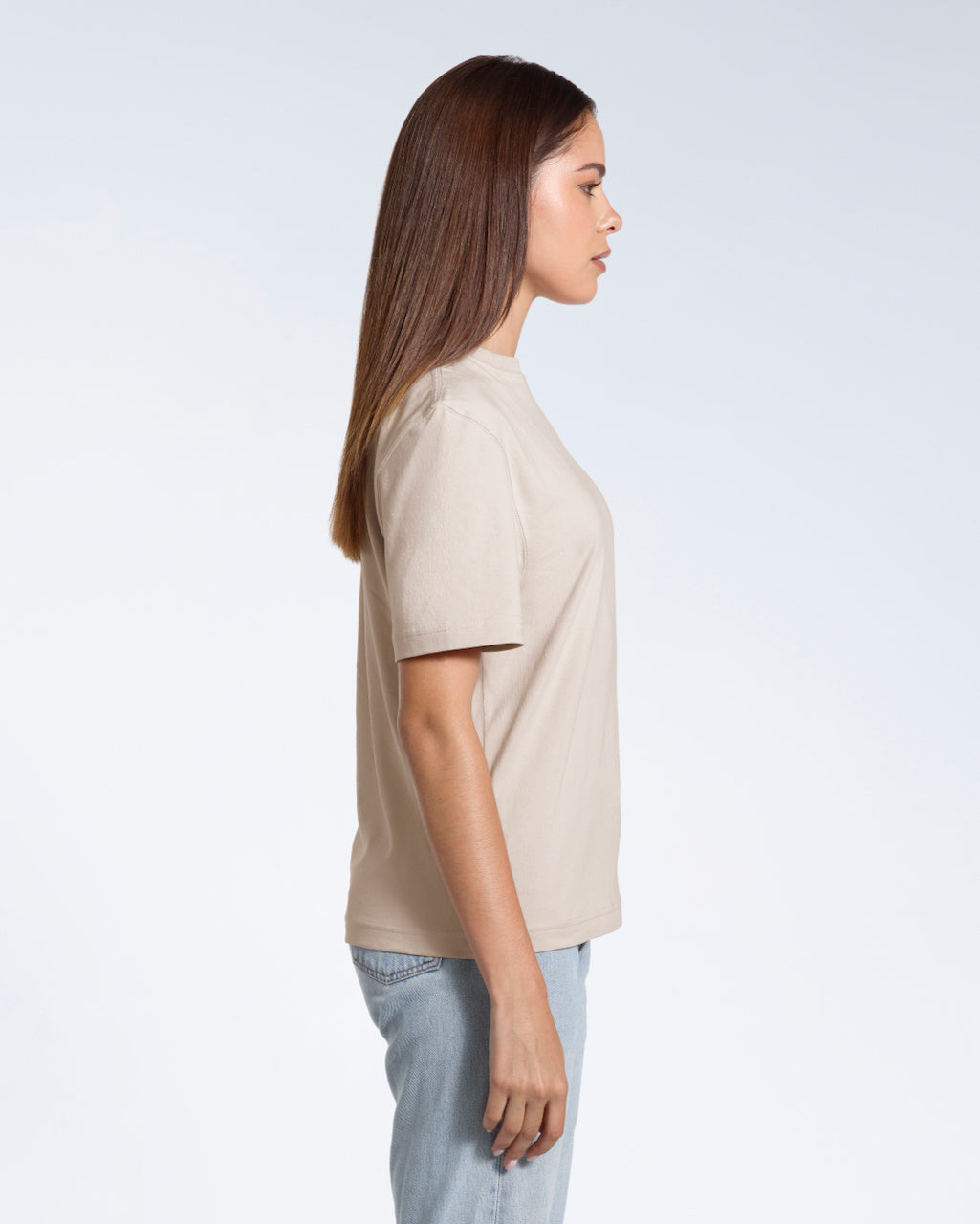 A woman facing side on, modelling a plain stone coloured short sleeve organic cotton t shirt.