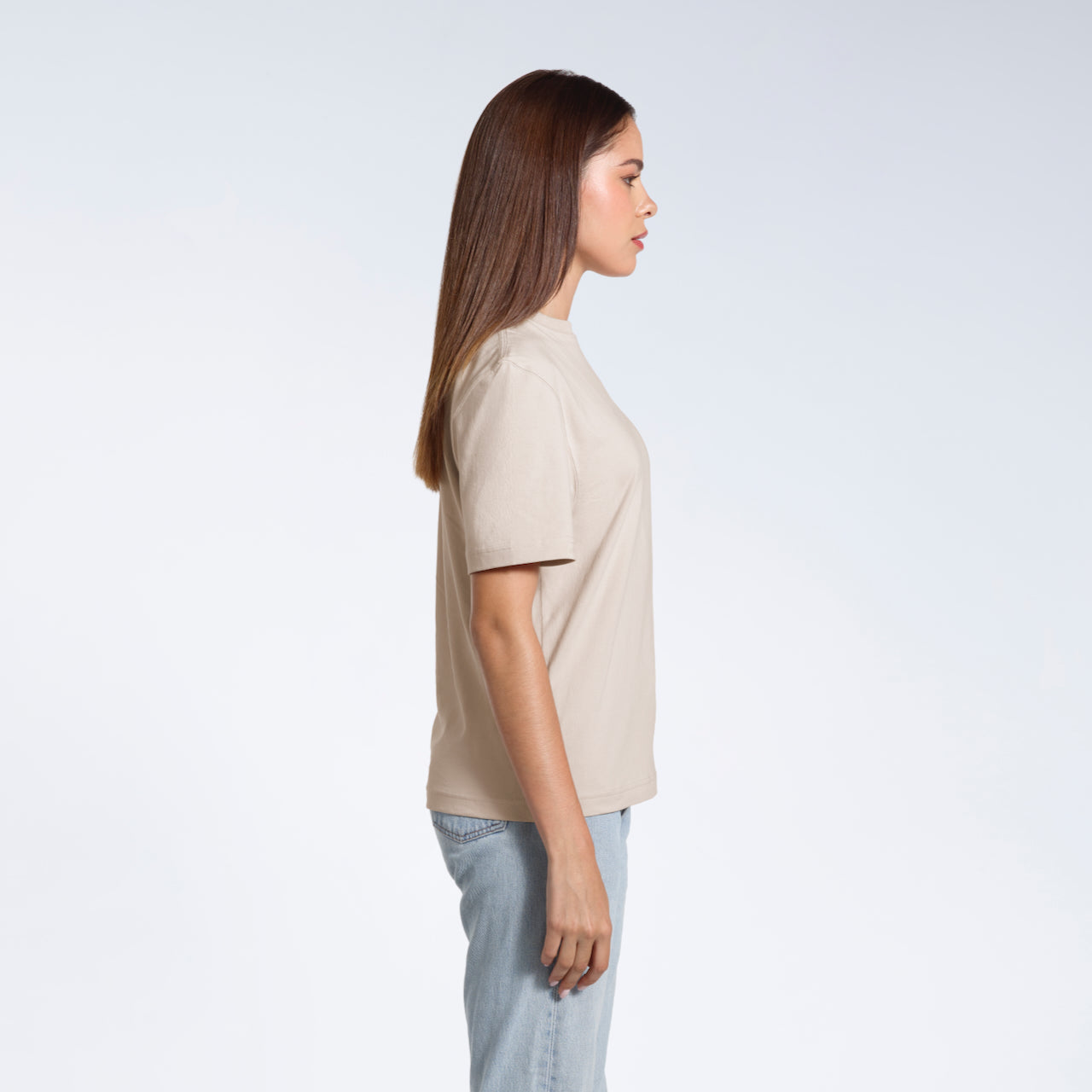 A woman facing side on, modelling a plain stone coloured short sleeve organic cotton t shirt.