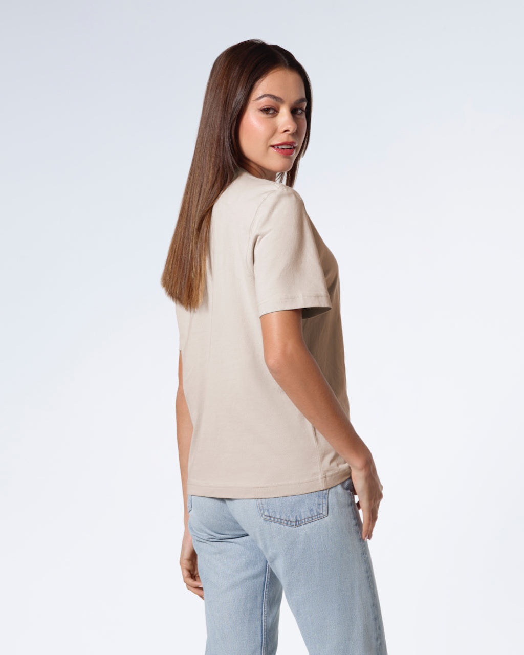A woman turned towards the camera smiling, modelling a plain stone coloured short sleeve organic cotton t shirt.