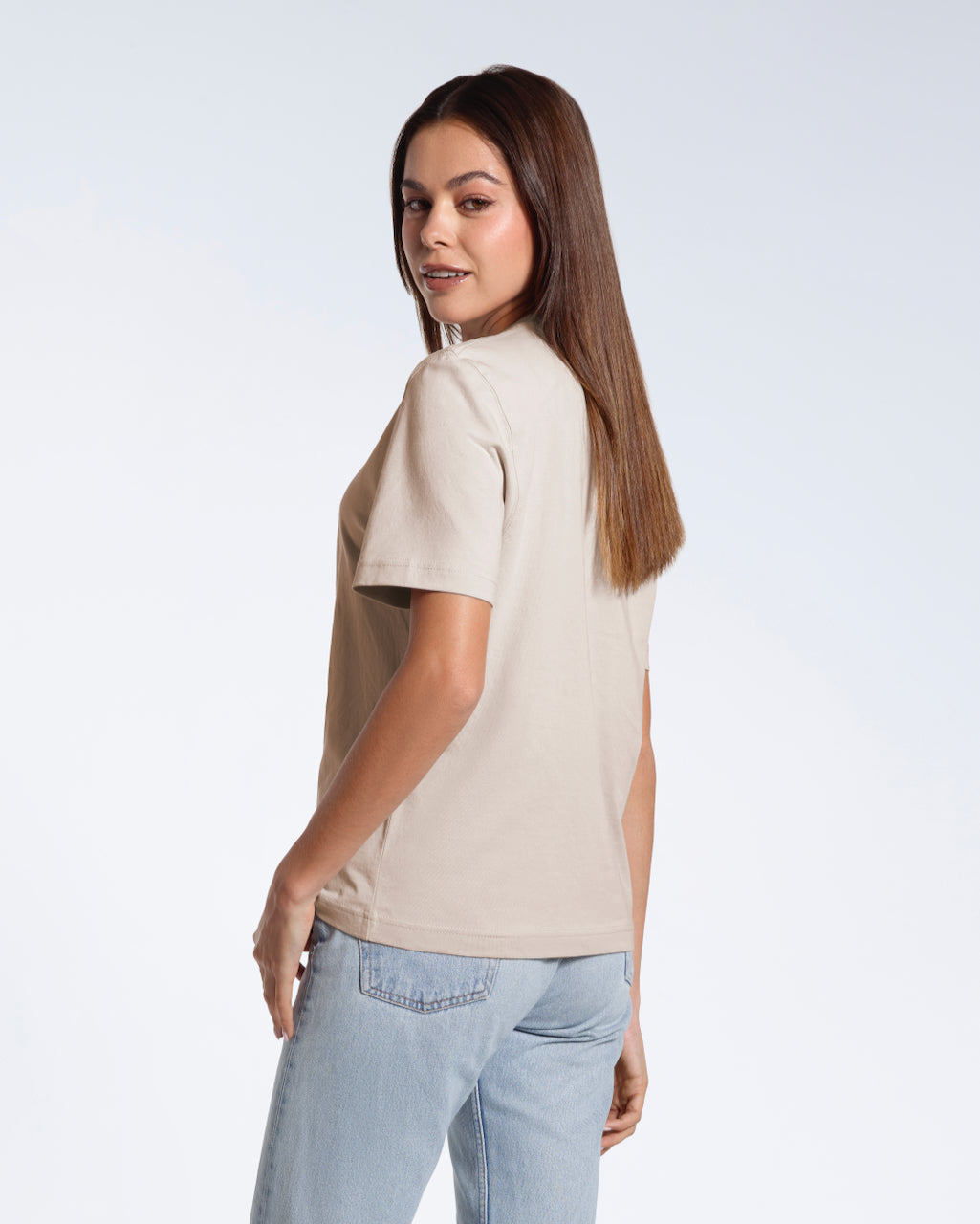 A woman turned towards the camera smiling, modelling a plain stone coloured short sleeve organic cotton t shirt.