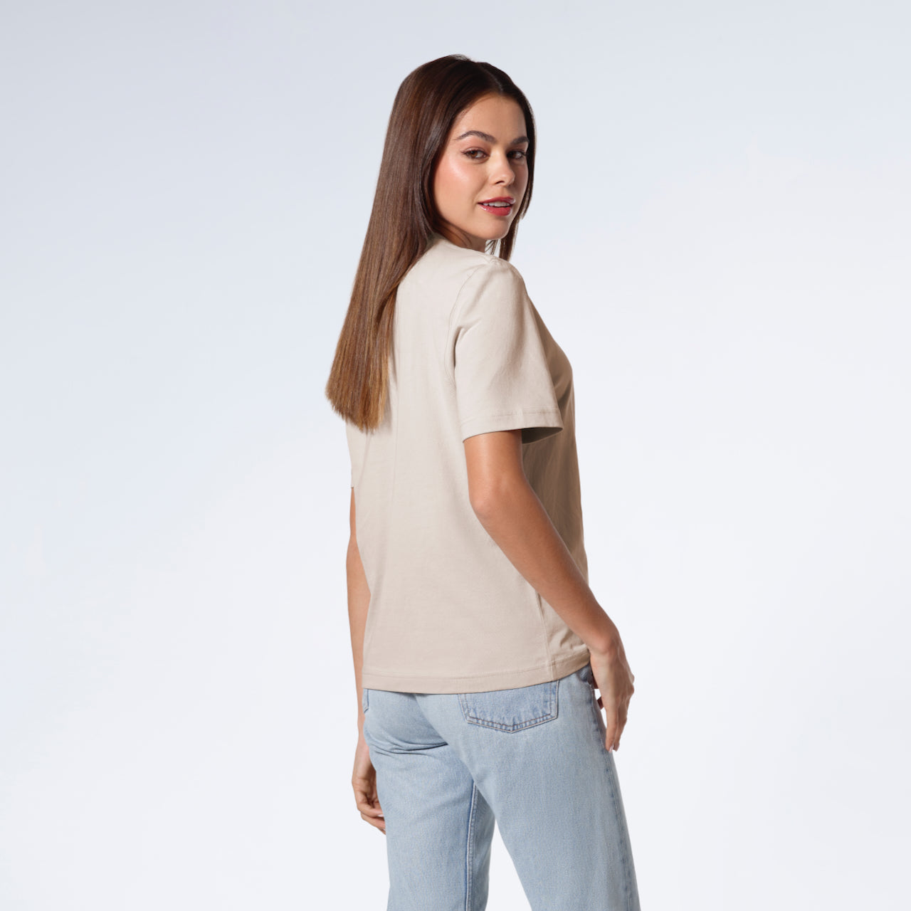 A woman turned towards the camera smiling, modelling a plain stone coloured short sleeve organic cotton t shirt.