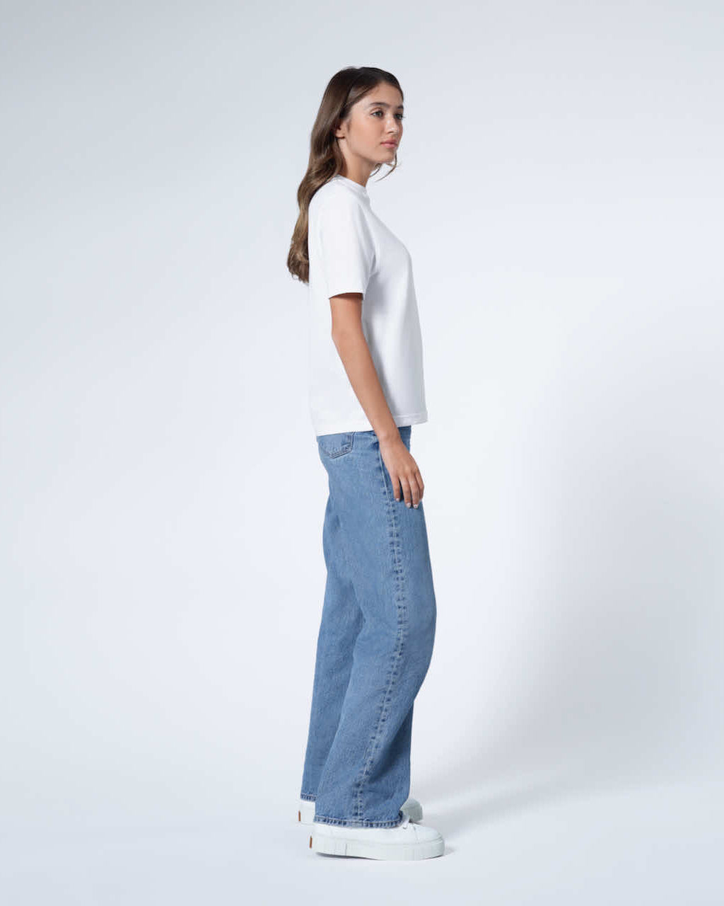 A woman facing side on, modelling a plain white short sleeve organic cotton t shirt.