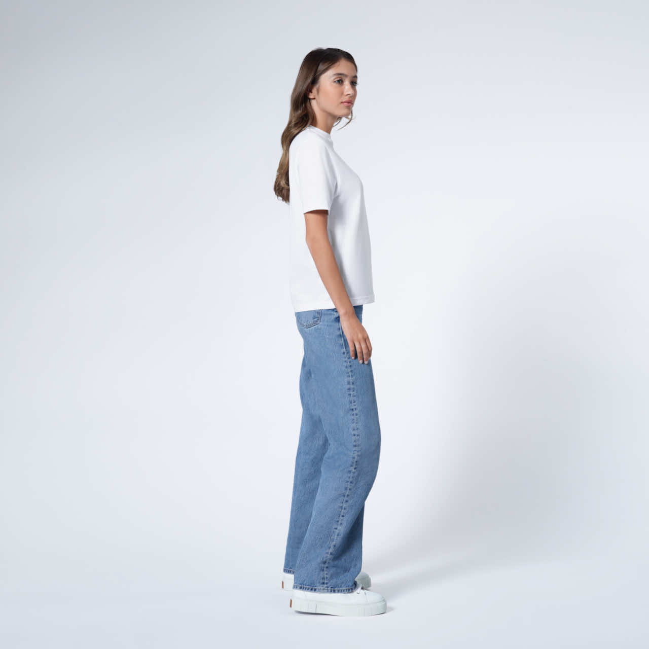 A woman facing side on, modelling a plain white short sleeve organic cotton t shirt.