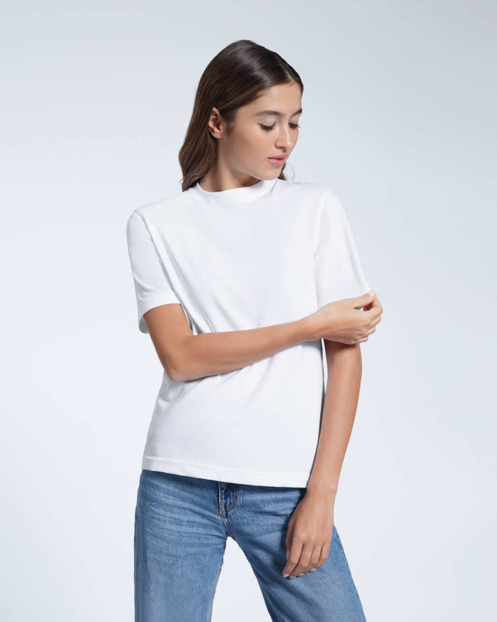 A woman looking down and touching her sleeve, modelling a plain white short sleeve organic cotton t shirt.