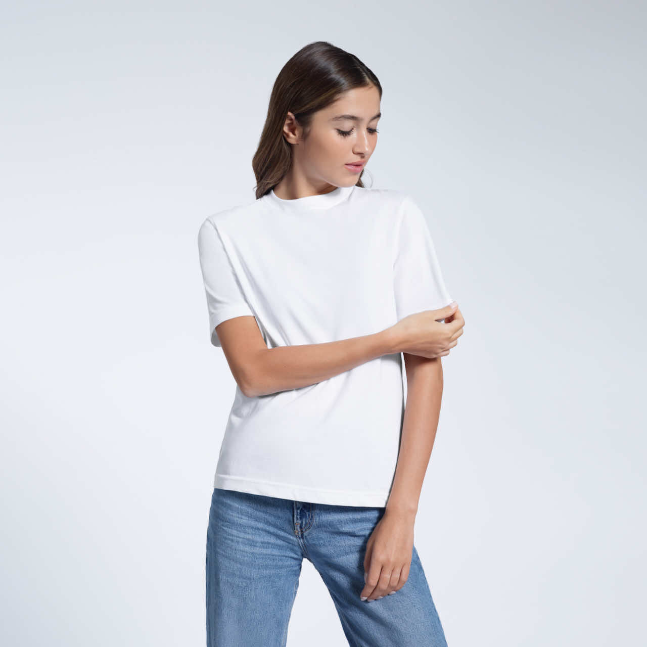 A woman looking down and touching her sleeve, modelling a plain white short sleeve organic cotton t shirt.