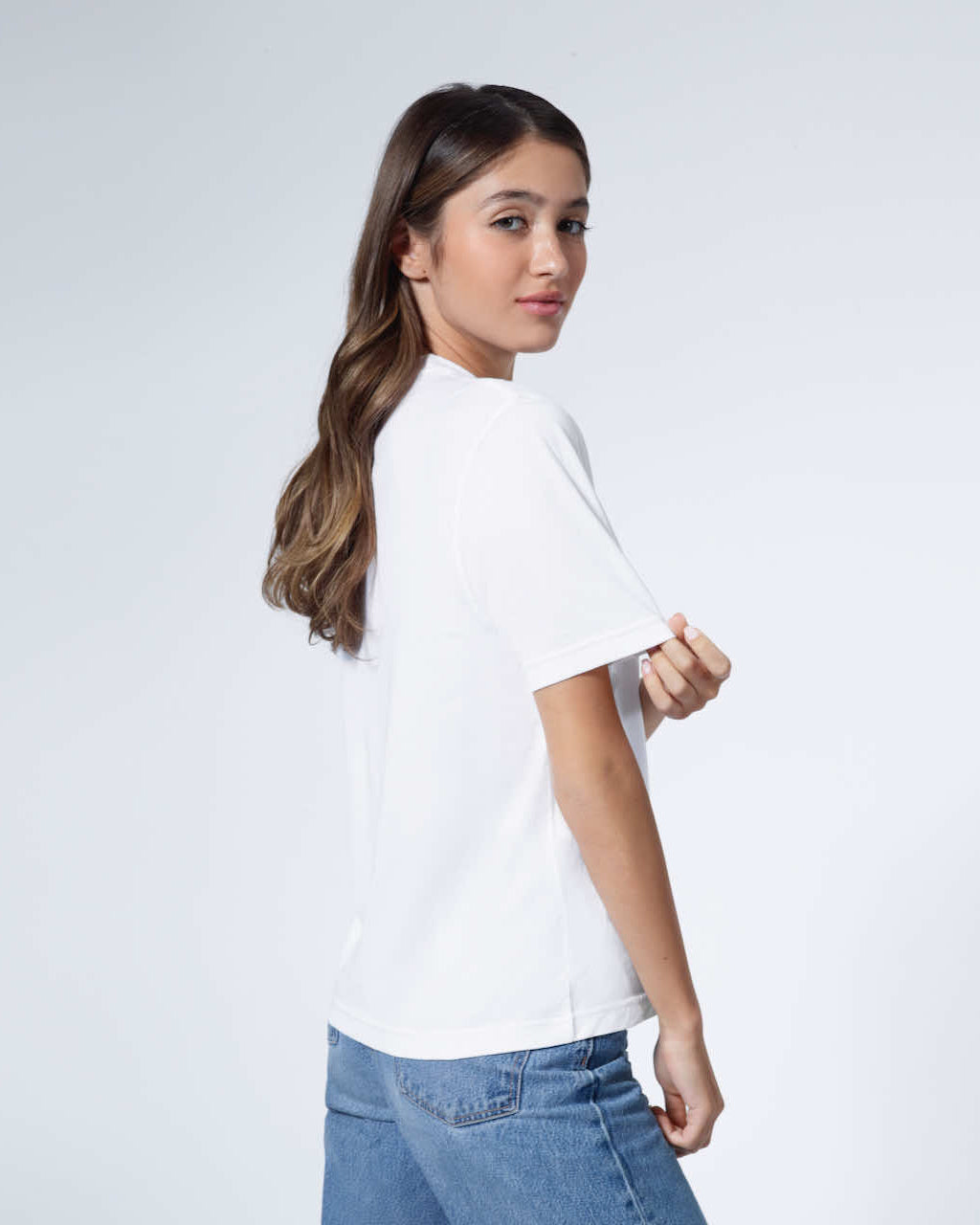 A woman looking back at the camera touching her sleeve, modelling a plain white organic cotton t shirt.