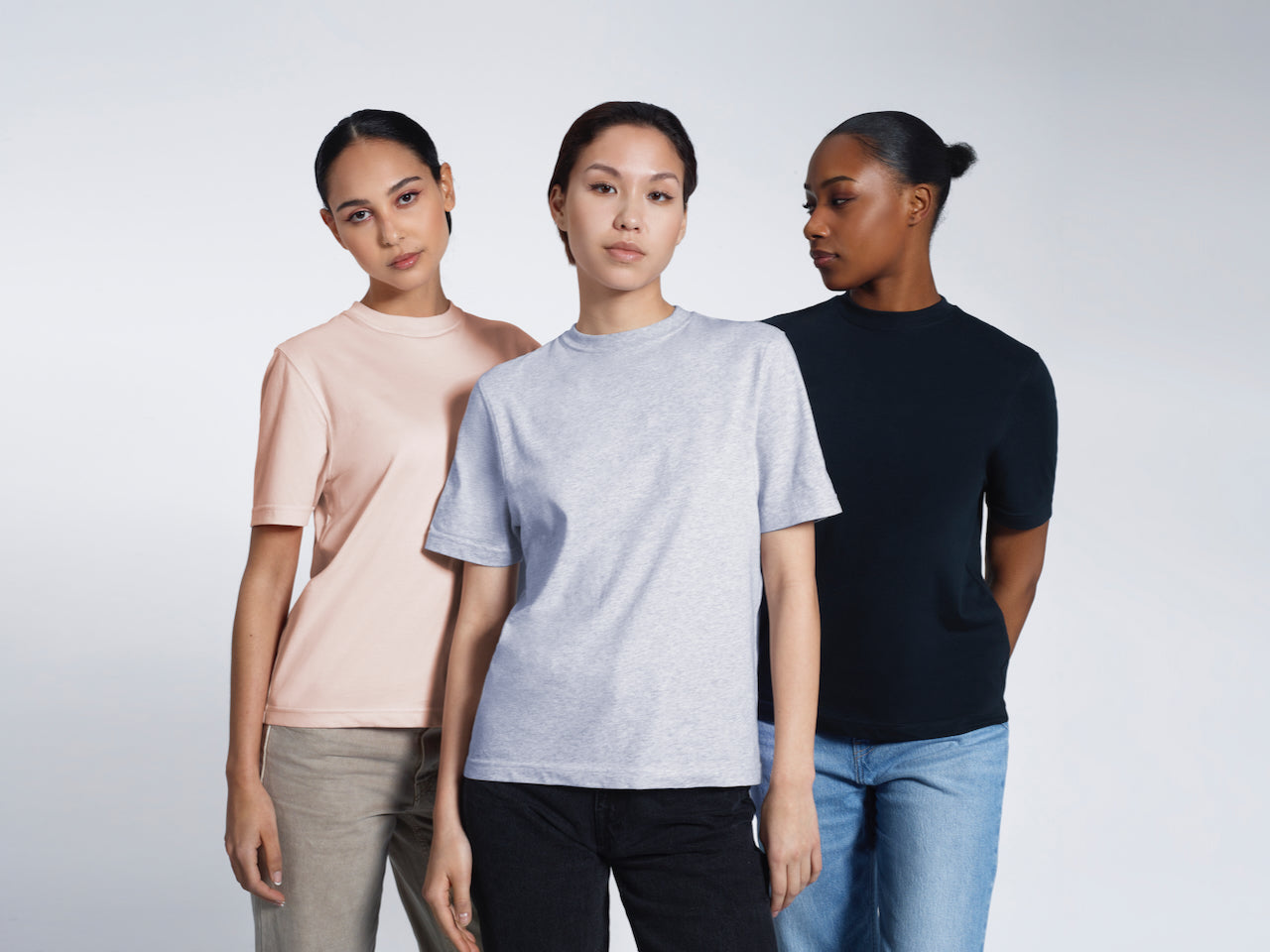Three women modelling plain grey, navy and pink organic cotton crew neck t shirts.