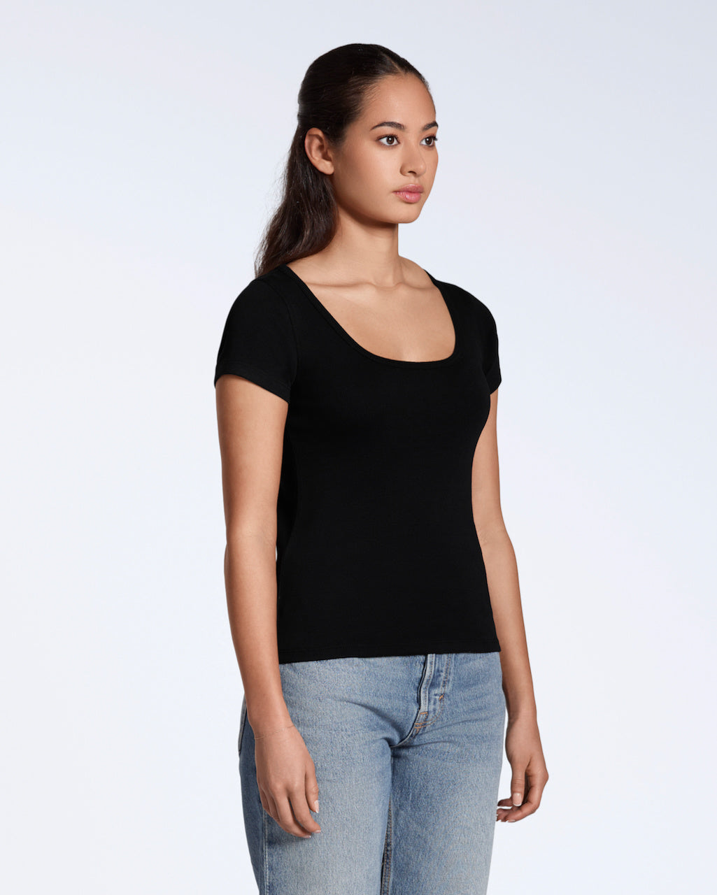 A woman looking away from the camera at an angle with her arms by her side, modelling a plain black, organic cotton scoop neck t shirt.
