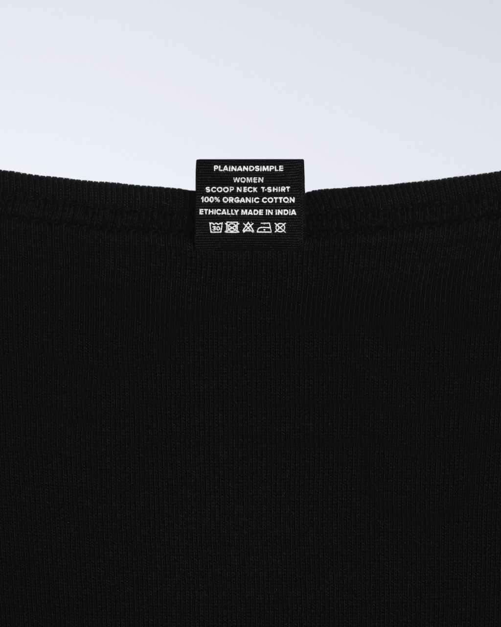 A close up of the neck label in a black, scoop neck, organic cotton polo shirt.