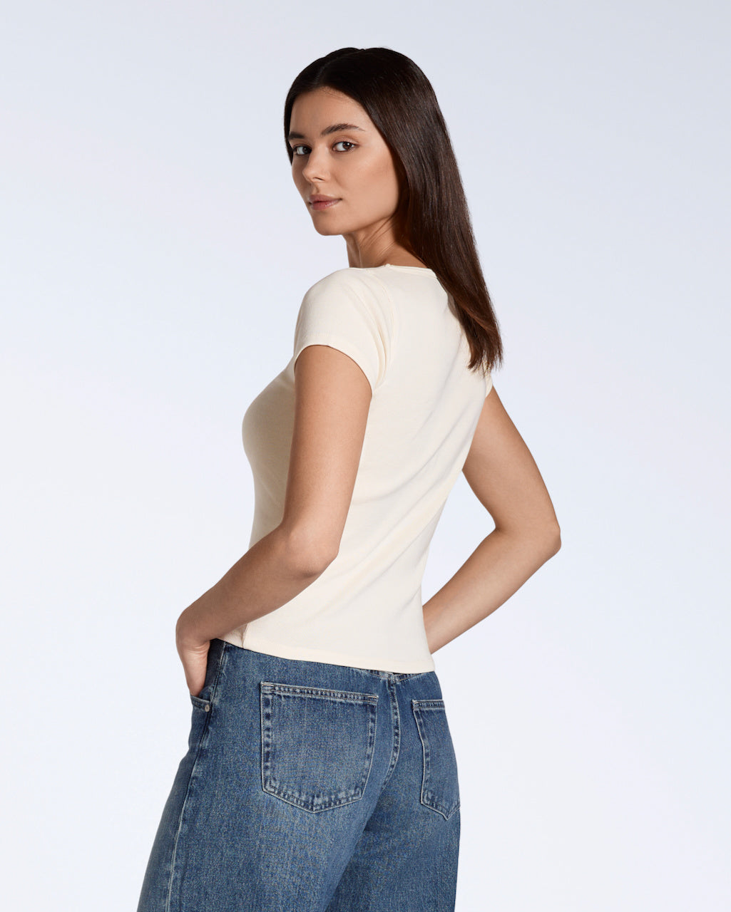 A woman looking over her shoulder to the camera, modelling a plain natural, organic cotton scoop neck t shirt.
