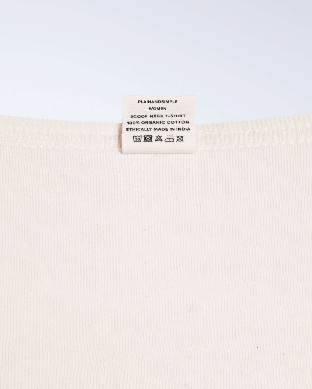 A close up of the neck label in a natural coloured, organic cotton, scoop neck t shirt.