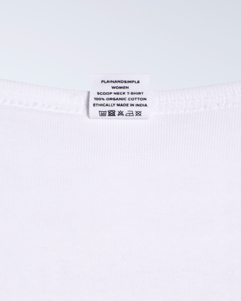 A close up of the neck label in a white, scoop neck, organic cotton polo shirt.