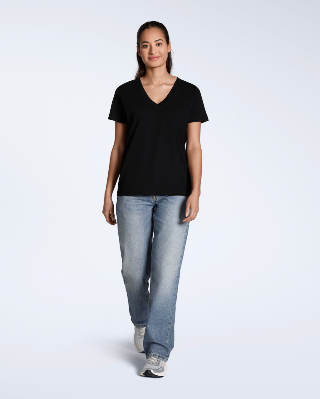 A full body photo of a woman smiling into the camera, modelling a plain black, organic cotton v neck t shirt with a pair of blue jeans.