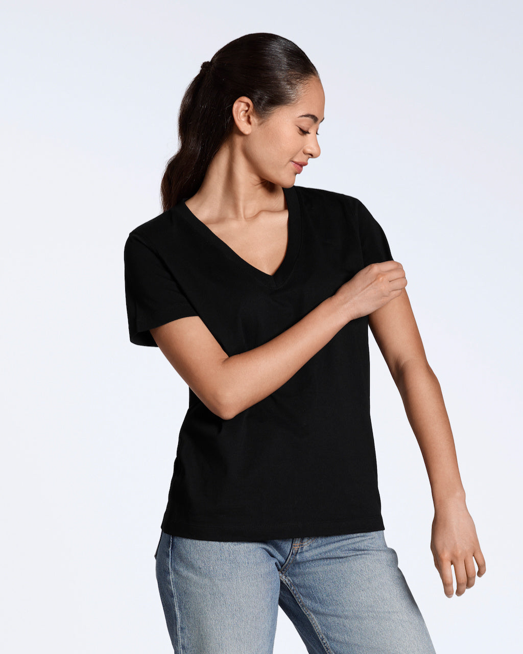 A woman looking down and touching her sleeve, modelling a plain black, organic cotton v neck t shirt with a pair of blue jeans.