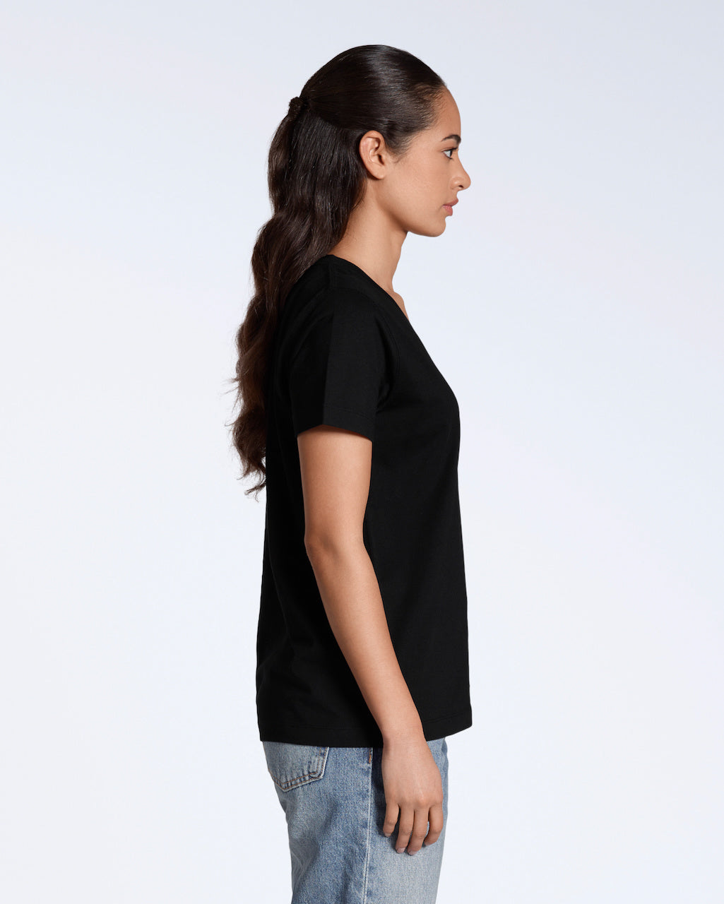 A woman facing side on, with her arms by her side, modelling a plain black, organic cotton v neck t shirt.