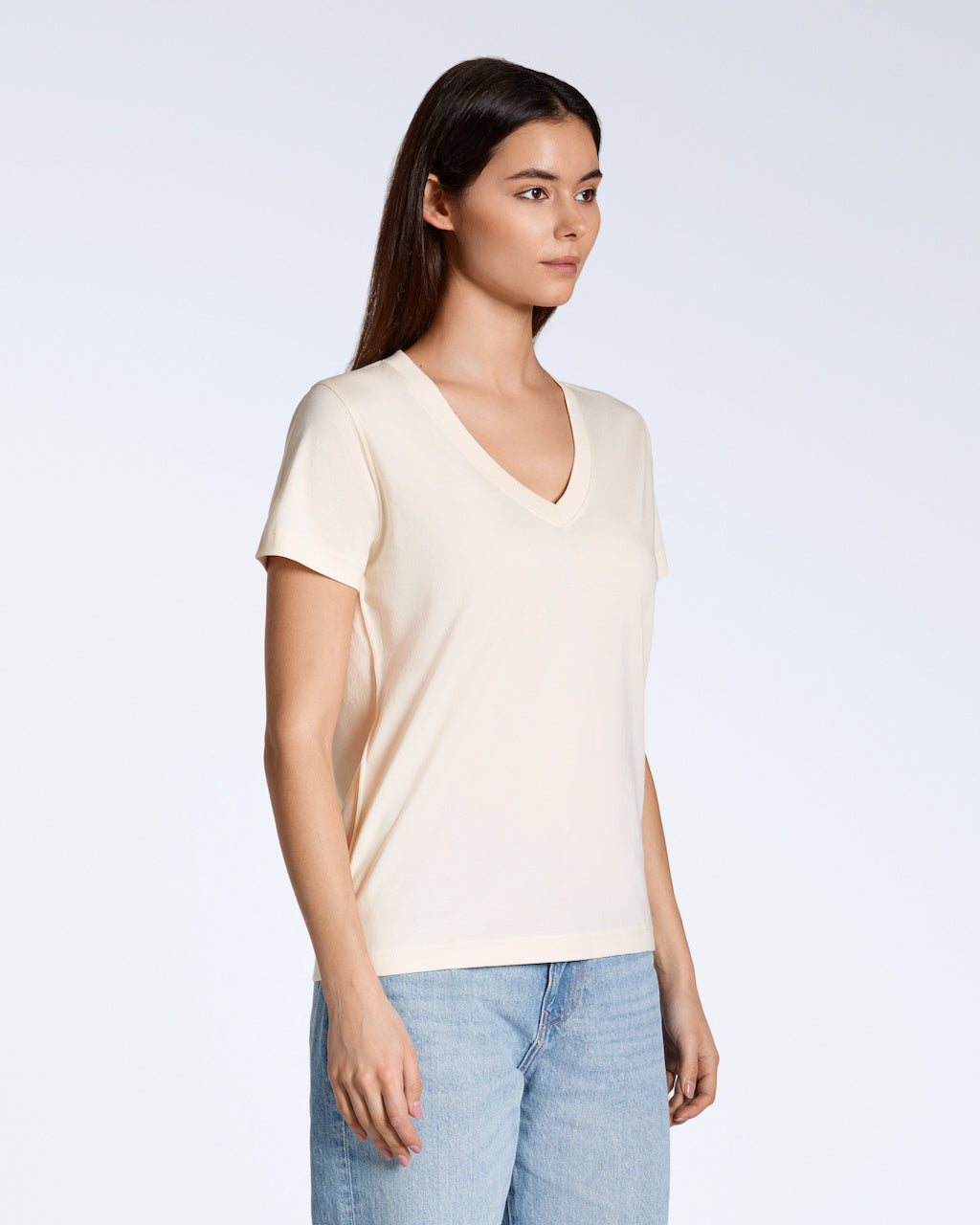 A woman looking away from the camera at an angle with her arms by her side, modelling a plain natural coloured, organic cotton v neck t shirt.