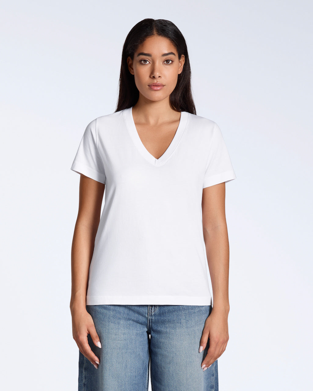 A woman facing front on, looking into the camera with her arms by her side, modelling a plain white, organic cotton v neck t shirt.