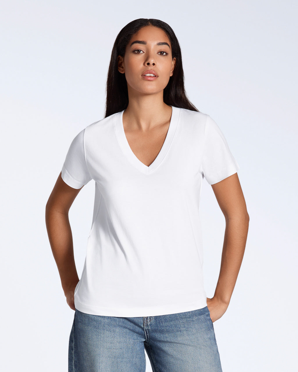 A woman looking into the camera with her hands by her hips, modelling a plain white, organic cotton v neck t shirt.