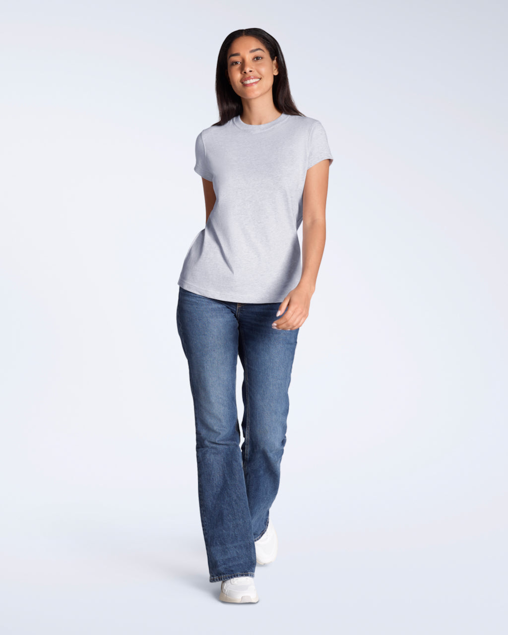 A full body photo of a woman smiling into the camera, modelling a plain grey, short sleeve organic cotton t shirt with a pair of jeans.