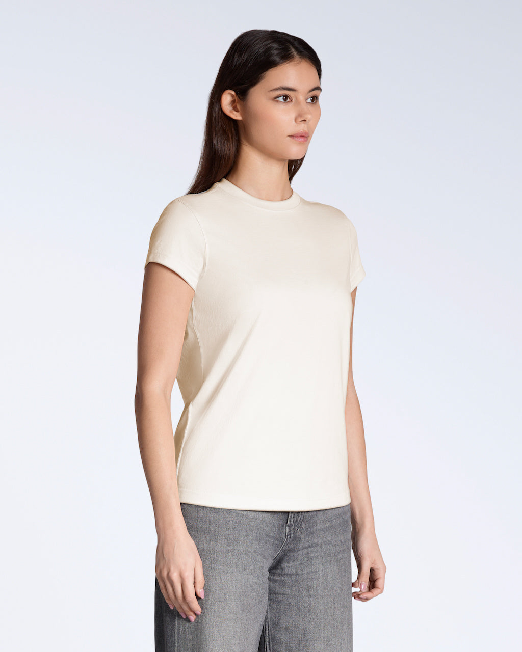 A woman at an angle with her arms by her sides, modelling a plain natural coloured, short sleeve organic cotton t shirt.