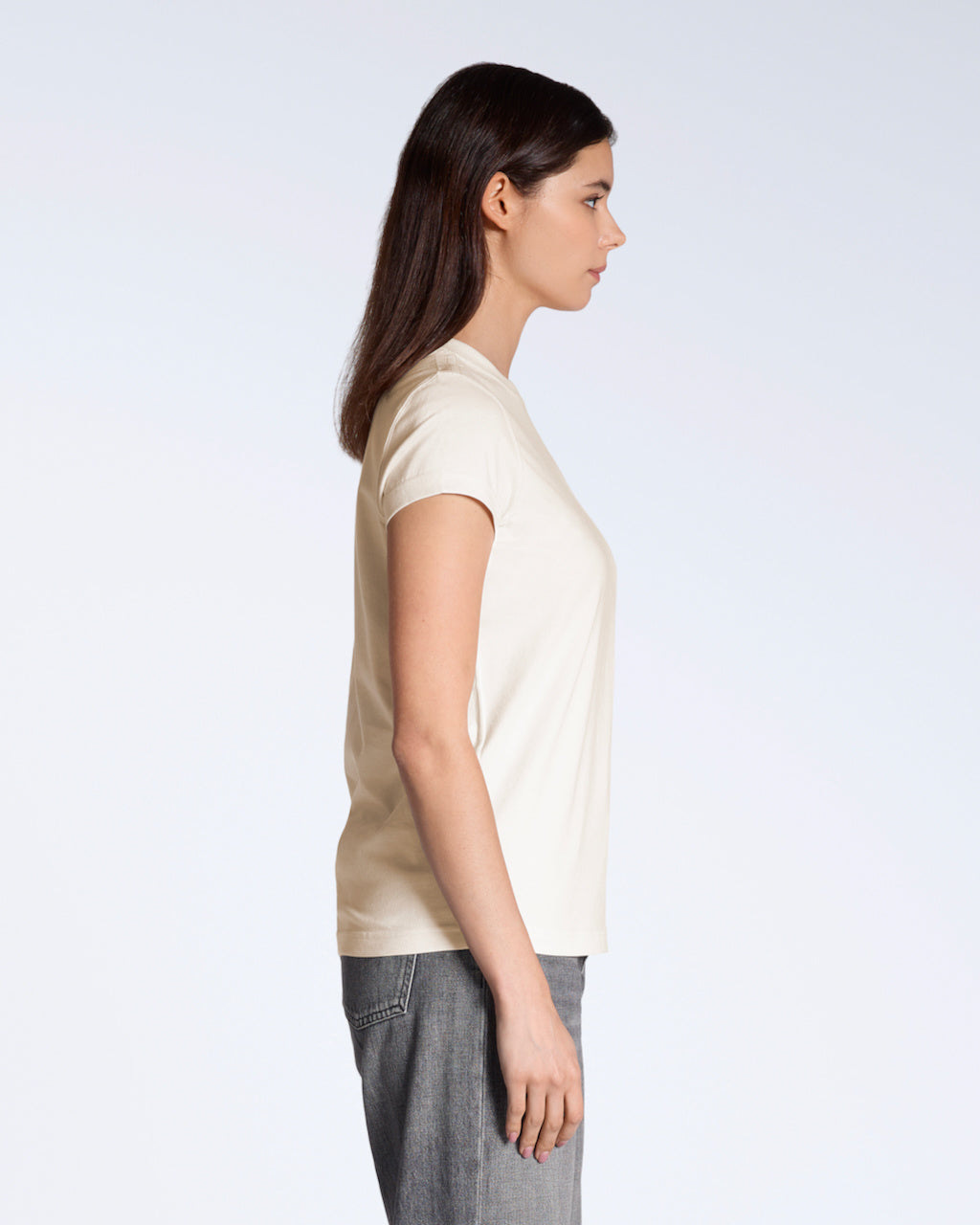 A woman facing side on, modelling a plain natural coloured, short sleeve organic cotton t shirt.