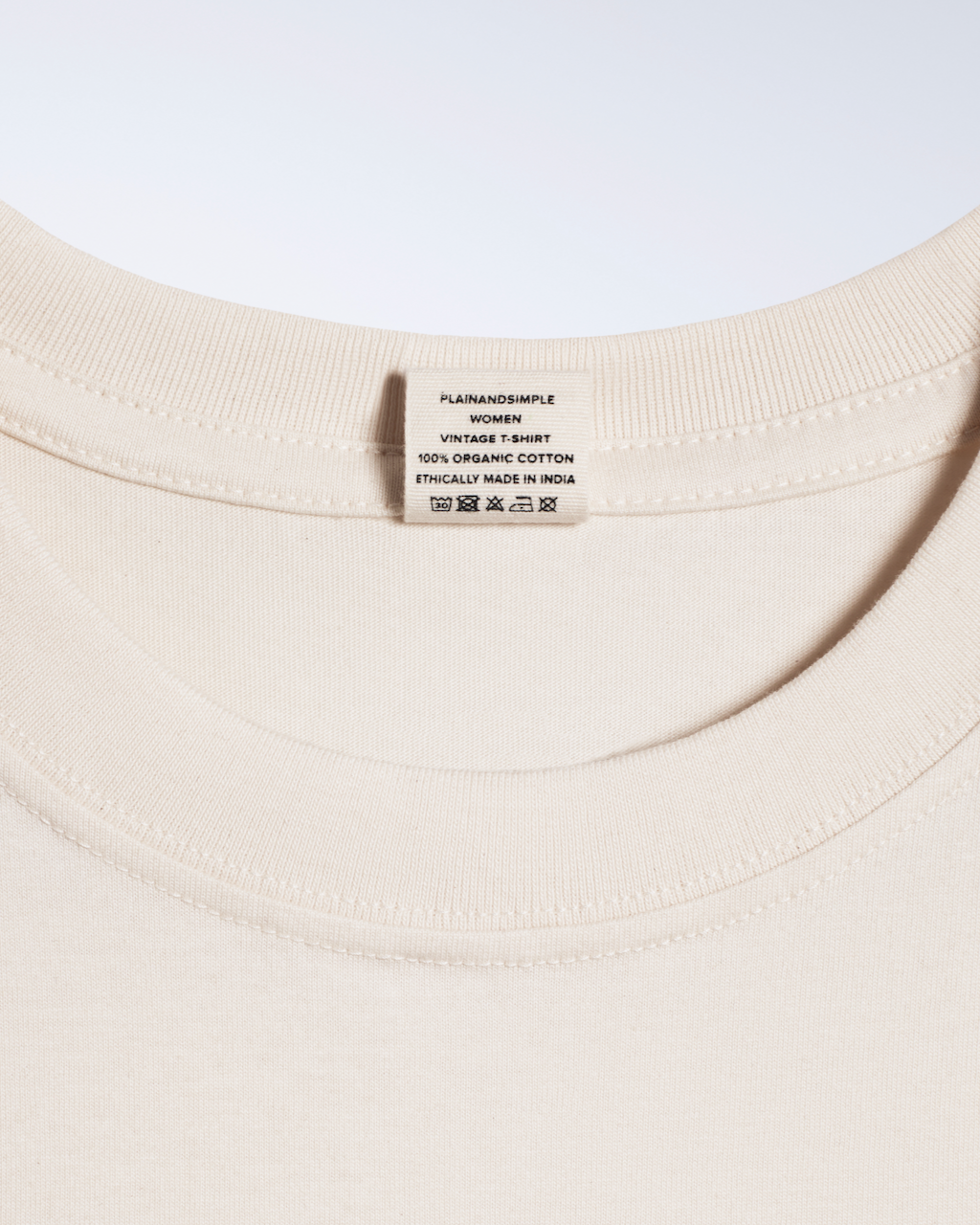 A close up of the neck label in a natural coloured, crew neck, organic cotton t shirt.
