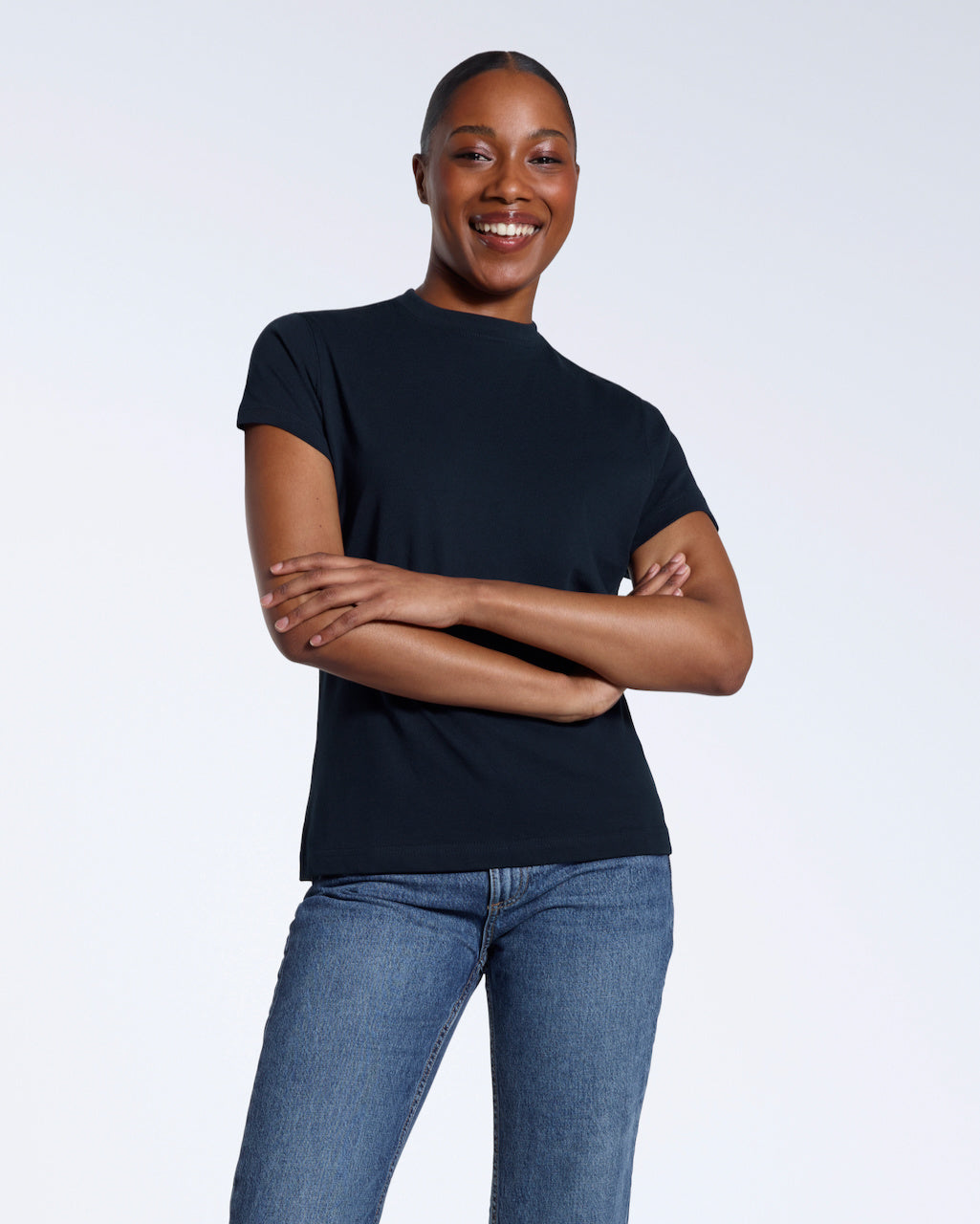 A woman smiling into the camera with her arms folded, modelling a plain navy short sleeve organic cotton t shirt.