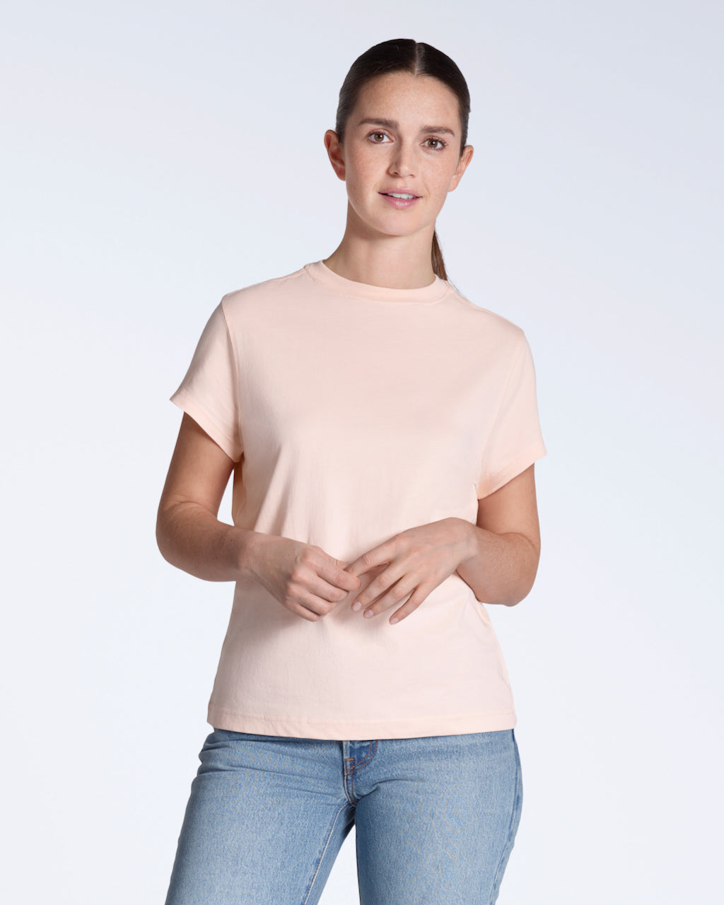A woman smiling into the camera, modelling a plain pink, organic cotton t shirt.