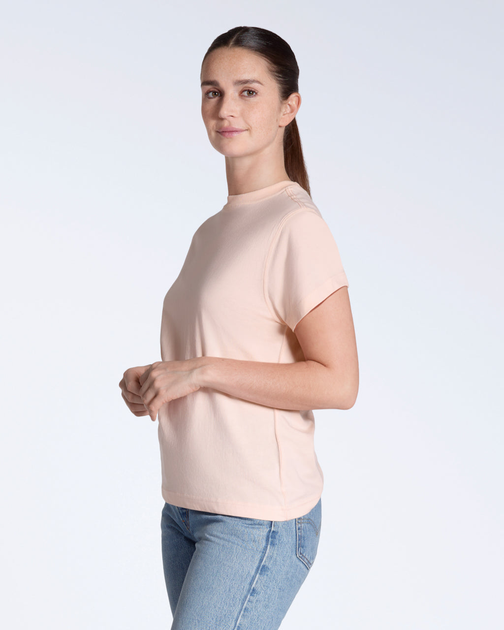 A woman smiling into the camera, modelling a plain pink, organic cotton t shirt.