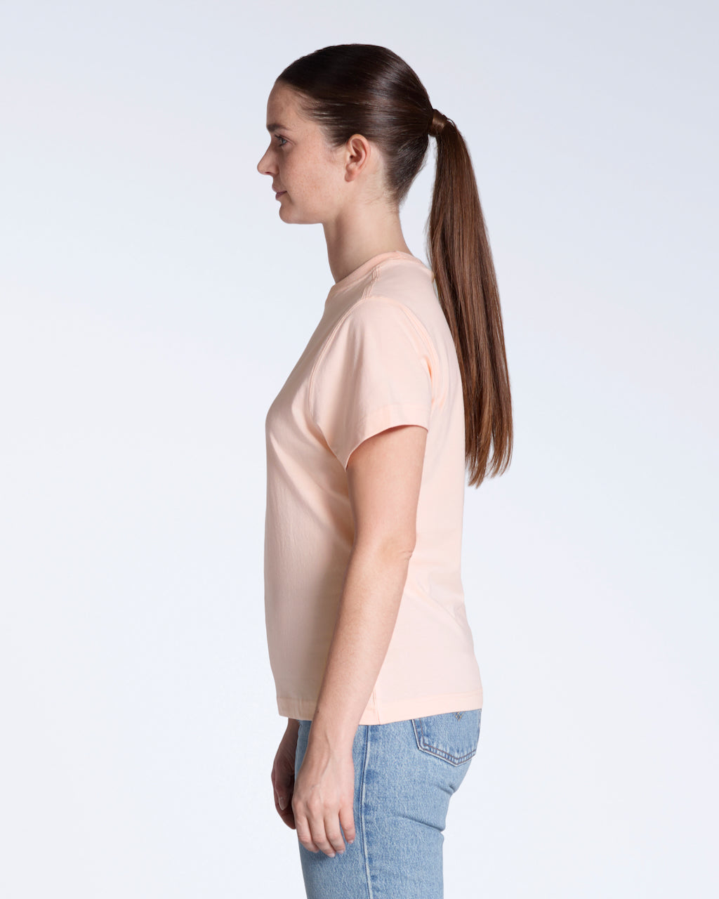 A woman facing side on, modelling a plain pink, short sleeve organic cotton t shirt.