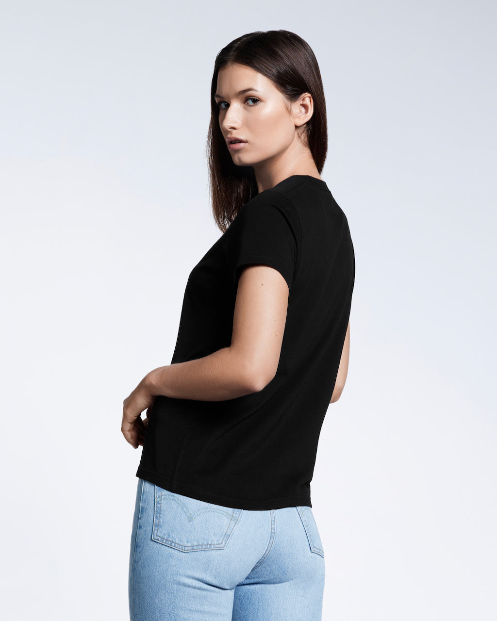 A woman turned to look at the camera modelling a plain black short sleeve organic cotton t shirt.