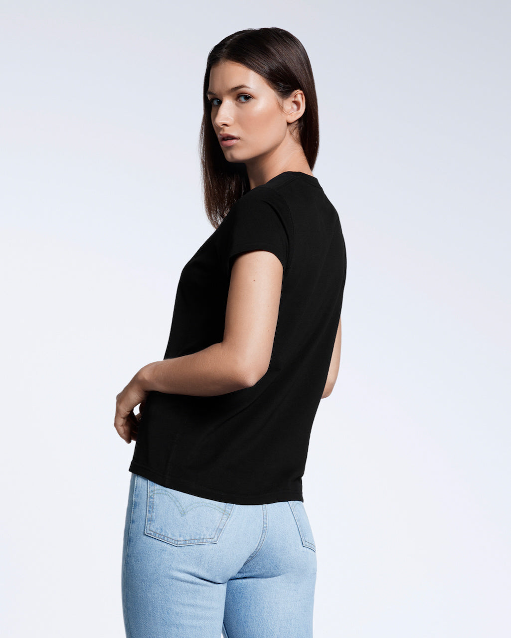 A woman turned to look at the camera modelling a plain black short sleeve organic cotton t shirt.