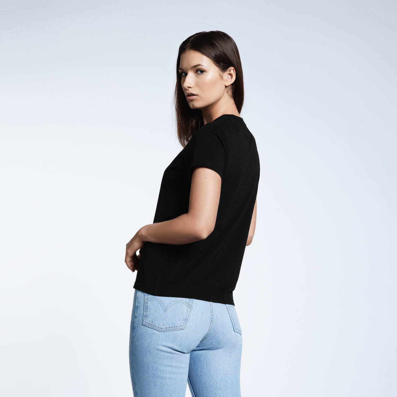 A woman turned to look at the camera modelling a plain black short sleeve organic cotton t shirt.