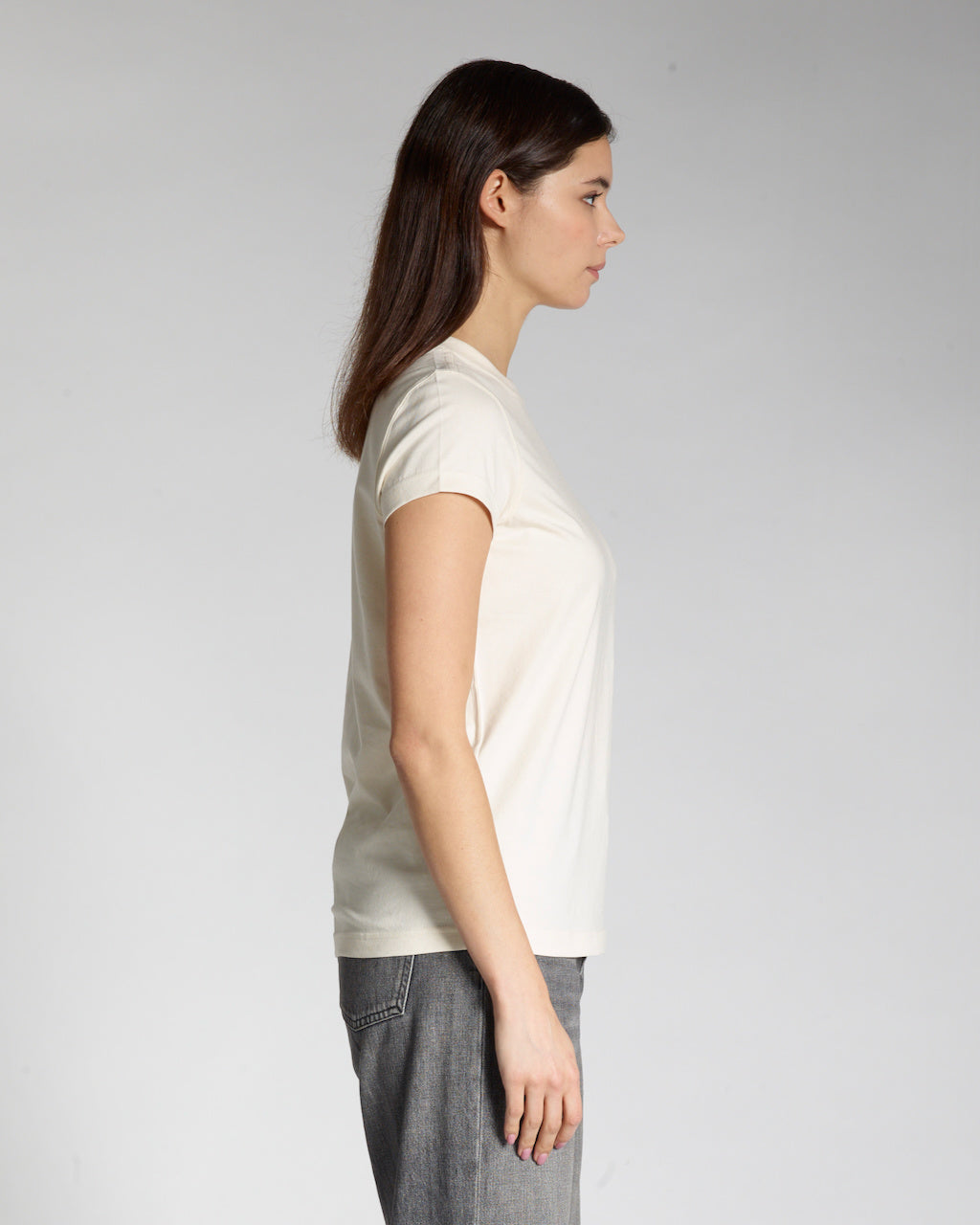 A woman facing side on, modelling a plain natural coloured, short sleeve organic cotton t shirt.