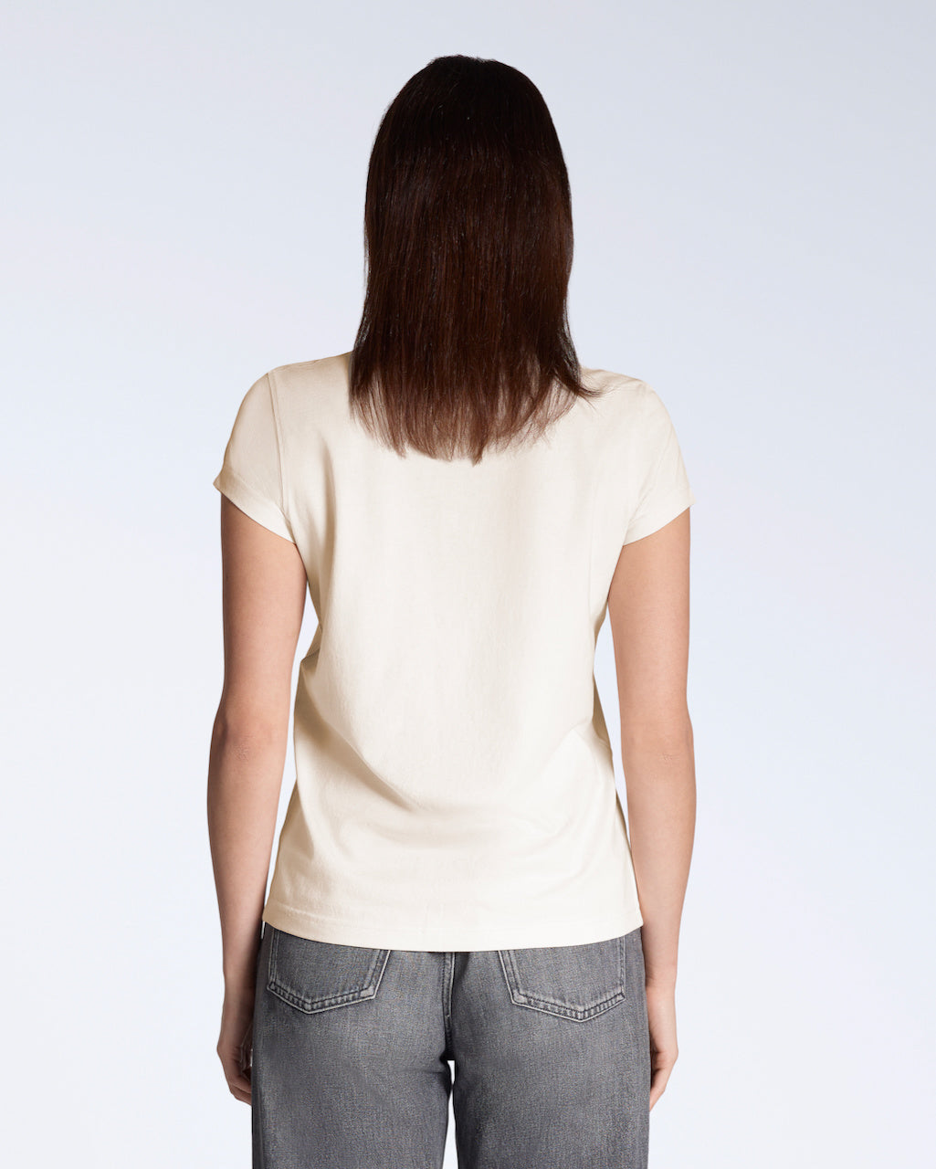 A woman facing away from the camera, modelling a plain natural coloured, short sleeve organic cotton t shirt.