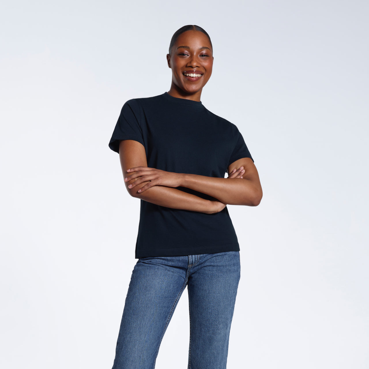 A woman smiling into the camera with her arms folded, modelling a plain navy short sleeve organic cotton t shirt.