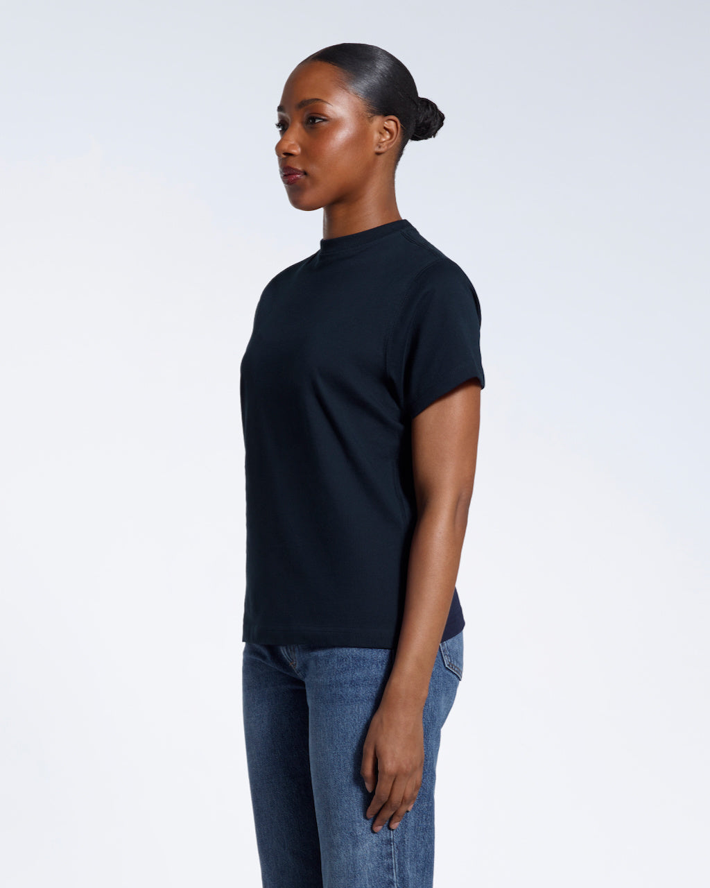 A woman looking away from the camera with her arms by her sides, modelling a plain navy short sleeve organic cotton t shirt.